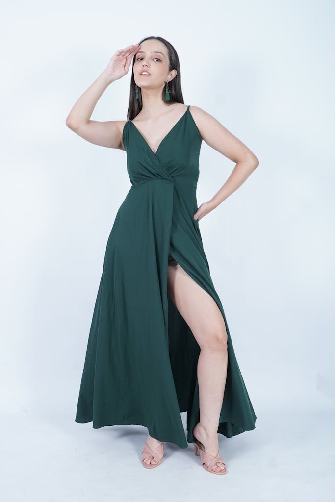 Fashionable woman in a long green dress posing elegantly in a studio setting.